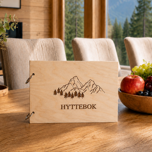 Hyttebok med gravert skog- og fjellmotiv på treomslag, vist med metallring på siden