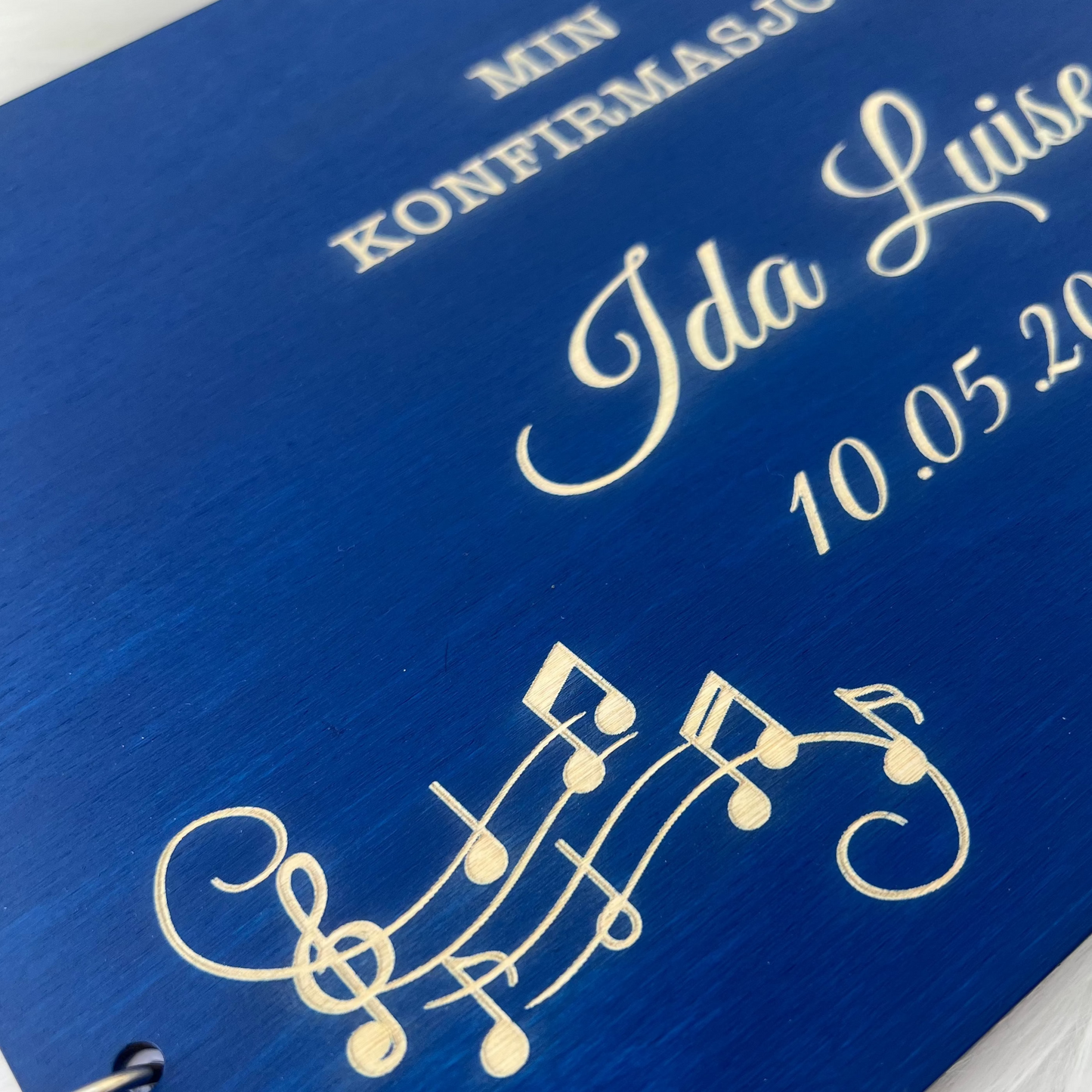 Nærbilde av detaljert musikkdesign gravert på et vakkert treomslag til konfirmasjon.