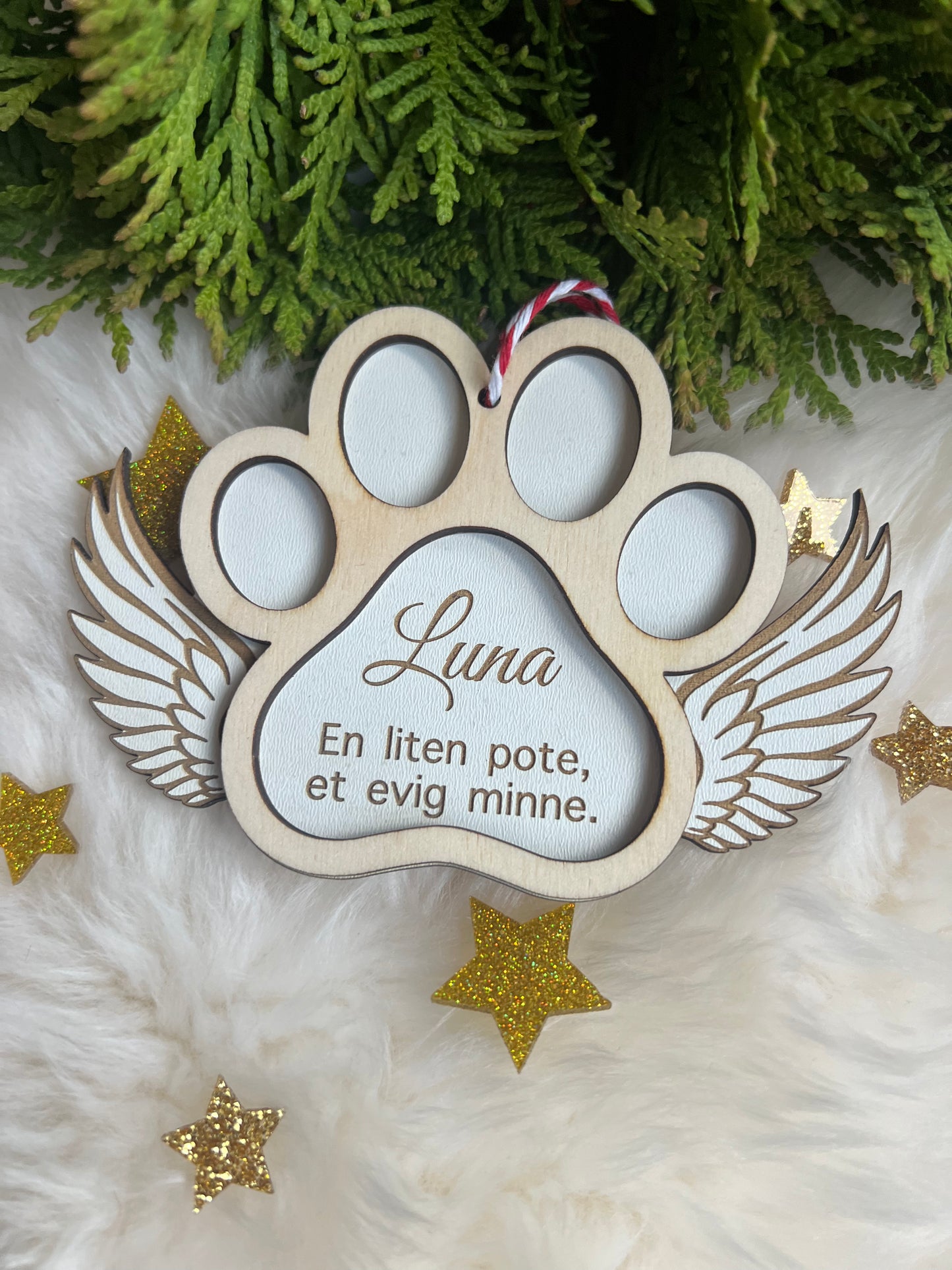 Minnesdekorasjon i poteform med tekst og vingedetaljer omgitt av stjerner.