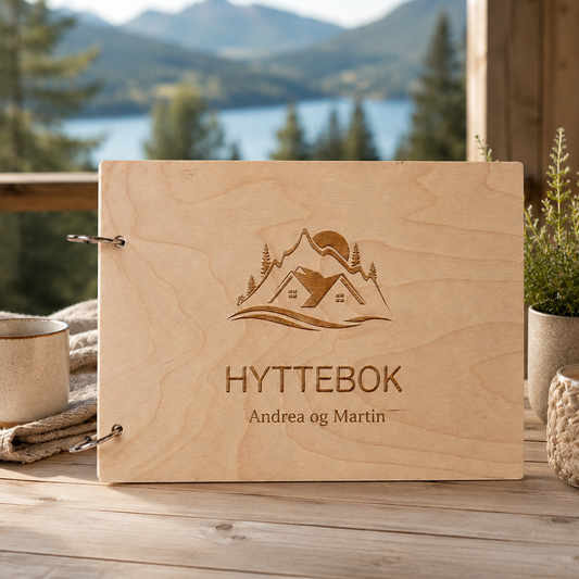 Hyttebok i lyst tre med personlig tekst og gravert hytte- og fjellmotiv på lukket omslag