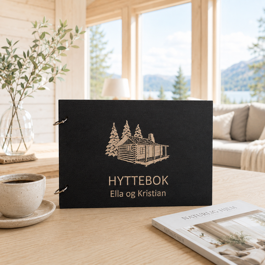 Svart personlig hyttebok med klassisk gravert hyttemotiv på lukket treomslag