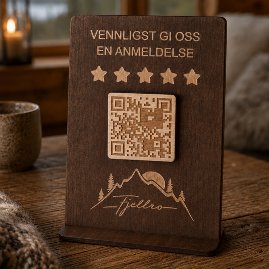 Treskilt med QR-kode og logo plassert ved siden av en hyttebok i tre på bordflate