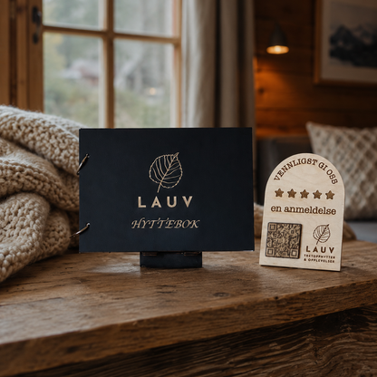Svart hyttebok med gravert logo og lite QR-skilt i tre plassert ved siden av boken